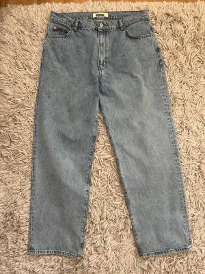 Woodbird Leroy Washed blue 34/30 - Ljusblå jeans från Woodbird med rak passform och klassisk femficksdesign. Jeansen har hög midja, gylf med knapp och dragkedja samt detaljer i silverfärgad metall. Tillverkade i 100% bomull för en autentisk denimkänsla. Storlek 34/30