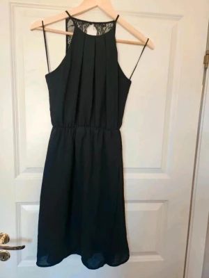 Klänning  Gina Tricot 34 - Svart klänning med tunna axelband och snygg spetsdetalj i ryggen. Klänningen har veckad front, markerad midja och faller i en mjuk, rak siluett. Perfekt för dig som gillar stilrena plagg med en twist.  E4