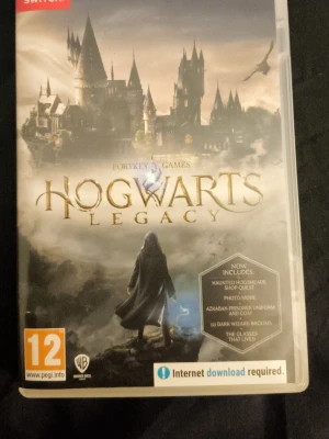 Hogwarts Legacy till Nintendo Switch - Hogwarts Legacy är ett actionrollspel till Nintendo Switch där du utforskar den magiska världen kring Hogwarts. Omslaget visar slottet och en trollkarl i kåpa. Spelet innehåller extra digitalt material som Haunted Hogsmeade Shop Quest och Azkaban Prisoner Uniform.