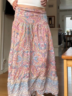 Färgglad långkjol med paisleymönster - Säljer en bohemisk långkjol i tunnt material med färgglatt paisleymönster i rosa, blått, gult och orange. Kjolen är bara använd några fåtal gånger!Kjolen har smock i midjan för skön passform och volang längst ner. Perfekt för dig som gillar färg och mönster! Säljer den eftersom att längden är lite för kort för min smak, men hade gärna behållit den eftersom att designen och mönstret är unikt och vackert! 
