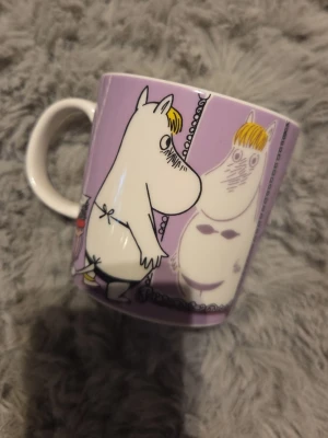 Lila Muminmugg med motiv - Säljer en lila mugg med motiv av Mumin-karaktärer.