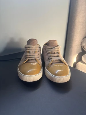Beige och bruna sneakers i mocka från lantvin  - Snygga sneakers i beige mocka med bruna, glansiga tåpartier och matchande beige snörning. Skorna har en klassisk låg profil och vit sula som ger en clean look. Perfekta för dig som gillar stilrena och neutrala färger.