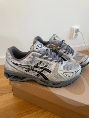 Asics Gel Kayano 14 - Snygga sneakers från Asics i silver och grått med svarta detaljer. Skorna har en sportig design med meshpaneler för bra ventilation och en robust sula för extra komfort. Perfekta för dig som gillar en modern och clean stil.