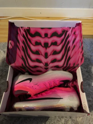 Nike rosa och vita fotbollsskor - Säljer ett par grymma fotbollsskor från Nike i en snygg rosa och vit färgkombination med svart swoosh. Skorna har en modern, strömlinjeformad design och genomskinlig sula med dobbar för bästa grepp på planen. Perfekta för dig som vill sticka ut på matchen!