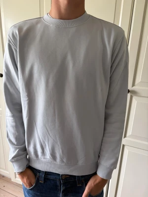 Ljusgrå basic sweatshirt - En stilren ljusgrå sweatshirt med rund hals och ribbade muddar vid ärmslut och nederkant. Tröjan har en enkel, clean design utan tryck eller mönster och är tillverkad i mjukt material som passar perfekt till jeans. Weekday helt ny i storlek S. Hör av er vid frågor och priset är inte hugget i sten!
