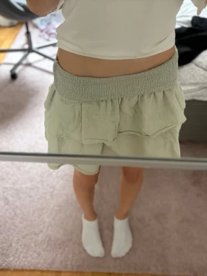 Grön volangkjol - Söt grön kortkjol med volangdetaljer. Kjolen har en avslappnad passform och är tillverkad i ett lätt material som passar perfekt till varma dagar. Enkel att matcha med olika toppar för en trendig look. Storleken är 146-152 men den är väldig stretchig så skulle säga den passar en XS super! Skriv om frågor!!🫶🏼
