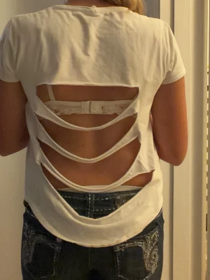 Vit t-shirt med öppen rygg - Säljer en vit t-shirt med korta ärmar och unik öppen rygg med flera horisontella utskärningar. Perfekt för dig som vill ha en edgy och trendig look. T-shirten har en normal passform. Man kan se blåa tushmarkeringar då jag klippt den själv men syns ej när man har på sig den. Strl 152 11/12 men kan nog även passa xs.  Tröjan är från Zara. Skriv vid frågor🌟