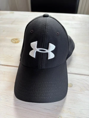 Sportig keps från Under Armour - Sportig och bekväm keps från Under Armour. Passar dig som har storlek M/L. Gummiband som resår vilket gör att den sitter extra bra på huvudet.