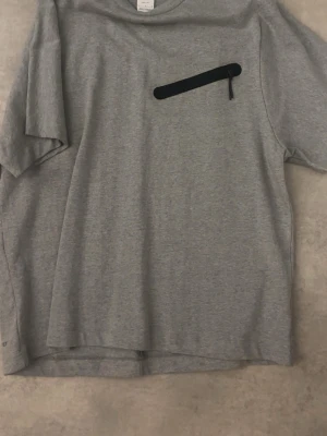 Grå Nike Dri-FIT t-shirt - Snygg grå t-shirt från Nike med Dri-FIT material som håller dig torr. T-shirten har en svart detalj på bröstet och klassisk rund hals. Perfekt för dig som gillar sportig och enkel stil.