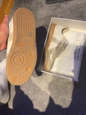Vita Masion Margiela  - Snygga sneakers i vitt och grått med klassisk gummisula. Skorna har mockadetaljer och vita partier i läder, samt vita skosnören. Perfekta för en clean och stilren look till vardagsoutfiten. Priset ej hugget i sten, dom är lite smutsiga kan fixa det innan de skickas. Dm för frågor!