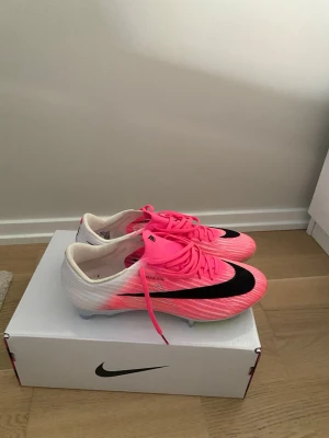 Nike Mercurial rosa/vita fotbollsskor - Säljer ett par Nike Mercurial fotbollsskor i färgen rosa och vit! Ett väldigt fint par fotbollskor som jag tyvärr behöver sälja pga storleken inte passade. Dem är endast använda 2 träningar och därmed är skicket nästan som nytt. Det kan man även se på bilden från undersidan av skon då det glansiga är kvar. Nypris ligger på 3500! 