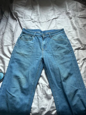 Ljusblåa raka jeans - Säljer ett par ljusblå jeans med rak passform och klassisk femficksdesign. Jeansen har normal midja och är tillverkade i denim med synliga sömmar. Perfekta för en avslappnad och trendig look.