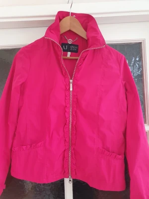 Armani jacka stl 42 - Mycket bra skick, sparsamt använt. Klar cerisefärgad. Längd 56cm, bredd armhåla-armhåla 51cm. 100% polyester. Är inte tyg utan mer som vindjackamaterial. Är normal 40 och varit bra passform för mig.