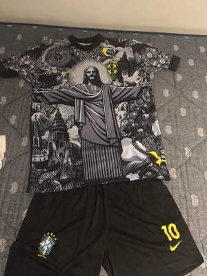 Brasilien Neymar Jr. matchställ svart - Säljer ett svart Brasilien matchställ med Neymar Jr. och nummer 10 på ryggen. Tröjan har ett stort tryck av Kristusstatyn och detaljer i gult och grått, samt brasilianska landslagets emblem. Shortsen är svarta med nummer 10 och CBF-logga. Perfekt för fotbollsträning eller fans.