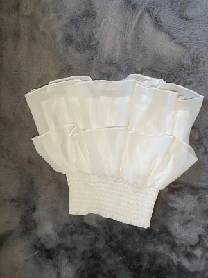 Vit volangkjol från Retro&Icone - Supersöt vit kjol från Retro&Icone i storlek XS. Kjolen har bred smock i midjan och flera lager volanger som ger en fluffig och trendig look. Perfekt för dig som vill ha en feminin och somrig stil.