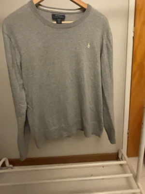 Grå tröja från Polo Ralph Lauren - Klassisk grå tröja från Polo Ralph Lauren med rund halsringning och diskret broderad logga på bröstet. Tillverkad i mjukt material och har långa ärmar samt ribbade muddar vid ärmslut och nederkant. Perfekt basplagg för alla tillfällen. Storlek xs. Skriv vid minsta fundering