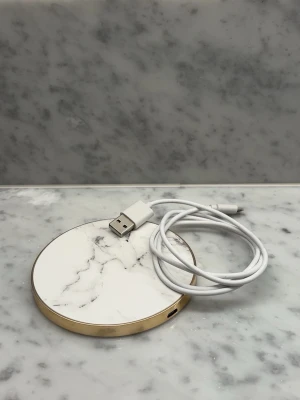 Trådlös laddningsplatta från Ideal of Sweden - Snygg trådlös laddningsplatta med vit marmordesign och guldfärgad kant. Medföljande vit USB-kabel, adapter medföljer ej. Passar de flesta mobiler som stödjer trådlös laddning 🩷