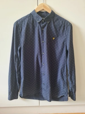 Mörkblå prickig skjorta från Lyle & Scott strl M - Fin mörkblå skjorta från Lyle & Scott med små vita prickar och klassisk krage. Skjortan har långa ärmar och knappar framtill. Material 100% bomull. Storlek M.