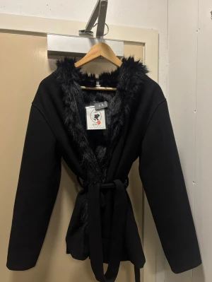 Svart kappa med fuskpäls och huva - svart päls kappa (inte äkta päls) den är liten i storleken så hade nog sagt att de ONE SIZED  och passar S M L finns två av dem i samma färg ifall de skulle vara mer som är intresserad hör av er om ni har frågor eller vill diskutera priset <3