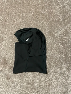 Riktig Nike ski mask  - Säljer en svart balaclava från Nike Pro med vit logga framtill. Tillverkad i ett stretchigt och funktionellt material som andas, perfekt för träning eller utomhusaktiviteter. Snygg och sportig design med synliga sömmar.
