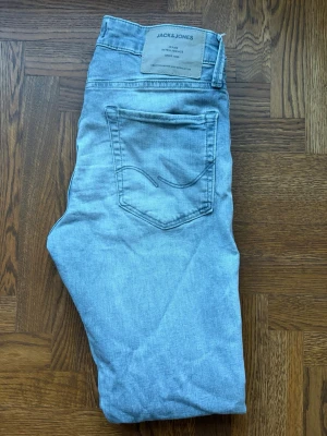 Ljusblå jeans från Jack & Jones - Snygga ljusgråa jeans från Jack & Jones med klassisk femficksdesign. Jeansen har en diskret bakficka med broderad detalj och är tillverkade i mjukt denimtyg. Perfekta för en avslappnad och trendig look. Storlek W28 L30