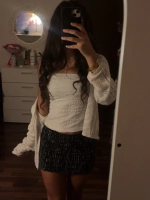 Svart kortkjol med vita ränder - Säljer en svart kortkjol med tunna vita ränder. Kjolen har en tight passform och är perfekt för dig som gillar en trendig och enkel stil. Passar till både stickade tröjor och crop tops.