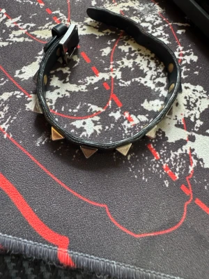 Mörkblått läderarmband med nitar från valentino - Säljer ett svart armband i läder med silverfärgade pyramidformade nitar längs hela bandet. Armbandet har ett spänne i metall för justering och ger en cool, edgy look. Perfekt för dig som gillar alternativ stil eller vill addera lite attityd till outfiten. Funkar bra, inga problem som jag märker med den, har varit använd så ha det i åtanke, kom med frågor om ni har! Har ej kvar påsen till det men man får med det i en andrahand påse istället!