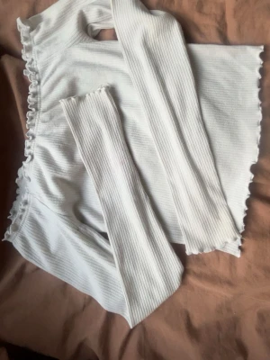 Vit ribbad topp från FB Sister - Säljer en vit långärmad topp från FB Sister i ribbat material. Tröjan har volangkant vid halsringning, ärmslut och nederkant för en söt touch. Perfekt att styla med jeans eller kjol för en trendig look.