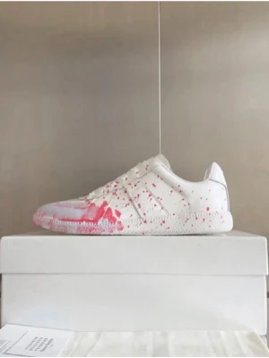 Vita sneakers med rosa färgstänk - Unika vita sneakers med rosa färgstänk över hela skon. Lågt skaft och klassisk siluett med snörning. Tillverkade i slätt läder för en clean look med en twist. Perfekta för dig som vill sticka ut med din stil. Skorna är liter mer använda än vad dom är på bilden men Frf extremt fräscha