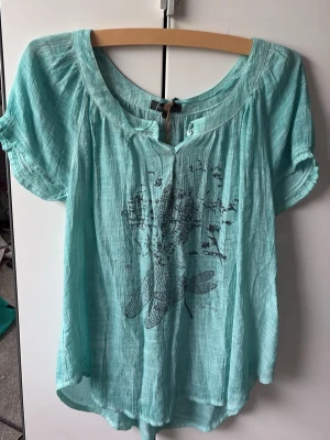 Turkos blus med trollsländetryck - Helt ny blus/t-shirt från Alice bizous. Aldrig använd. Köpte den men den va lite för stor för mig. Storlek M. Älskar den. Men måste tyvärr sälja den då jag råka köpa förstor storlek! Prislapp kvar + en liten påse med en knapp ifall en knapp lossnar🔥