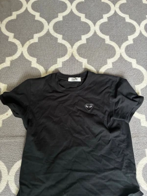 Svart t-shirt med hjärtdetalj - Snygg svart t-shirt med ett litet hjärta broderat på bröstet. Klassisk rund hals och korta ärmar. Perfekt basplagg som funkar till det mesta och är enkel att matcha med andra plagg.