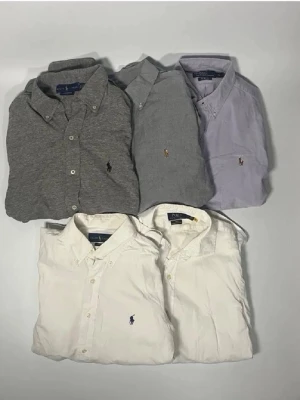 Klassiska skjortor från Polo Ralph Lauren - Fem skjortor från Polo Ralph Lauren i grått, ljusgrått, ljuslila och vitt. Alla har button-down krage, broderad logga på bröstet och knappar framtill. Perfekta för en clean och stilren look. Storlek M och en S 