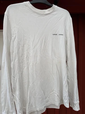 Vit långärmad t-shirt Samsøe Samsøe - Klassisk vit långärmad t-shirt från Samsøe Samsøe med diskret logga på bröstet. Tröjan har rund halsringning och är gjord i mjuk bomull som känns skön mot huden. Perfekt basplagg för alla tillfällen och enkel att matcha med olika stilar.