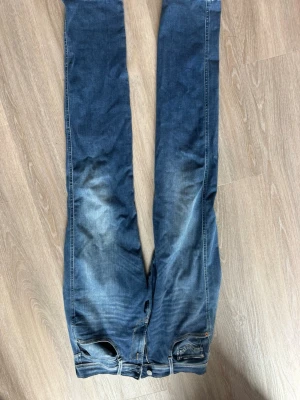 Blå jeans från ANBASS, storlek 31 - Säljer ett par blå jeans från ANBASS i storlek 31. Jeansen har en klassisk femficksmodell, smal passform och snygga slitningar framtill för en trendig look. Perfekta till sneakers och hoodie för en avslappnad stil.