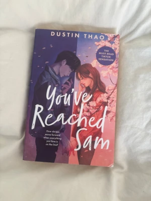 You've Reached Sam av Dustin Thao - En ungdomsroman med ett omslag i lila och rosa toner, prydd med illustration av två tonåringar och körsbärsblommor. Boken handlar om kärlek, förlust och att få en andra chans att säga hejdå. Perfekt för dig som gillar känslosamma berättelser och TikTok-hajpade böcker.