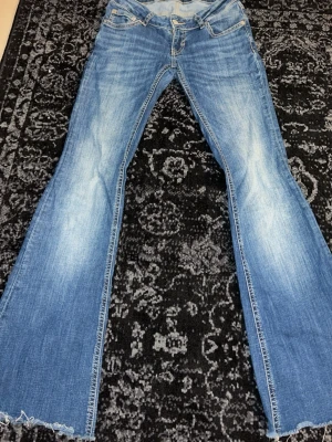 Blå bootcut jeans med slitna detaljer - Säljer ett par mörkblåa bootcut jeans med slitningar och fransad nederkant. Jag har klippt jeansen och jag är 165cm lång och dom är på gränsen för mig på längden 