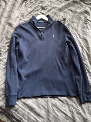  Polo Ralph Lauren zip - Snygg marinblå långärmad tröja från Polo Ralph Lauren med klassisk quarter zip och broderad logga på bröstet. Tillverkad i mjukt bomullsmaterial och har ribbade muddar vid ärmslut och nederkant. Perfekt för en clean och stilren look.