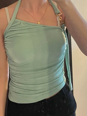 Ljusgrön omlott halterneck topp - Trendig ljusgrön topp med omlott-detalj och halterneck. Toppen har smala axelband och är figurnära med snygga rynkningar längs sidorna. Perfekt för dig som vill ha en unik och stilren look.