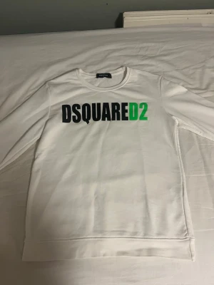 Vit sweatshirt från Dsquared2 - Säljer en clean vit sweatshirt från Dsquared2 med stor svart och grön logga på bröstet. Tröjan har rund halsringning och långa ärmar. Perfekt för dig som gillar stilrena plagg med tydlig branding. Materialet känns mjukt och bekvämt.