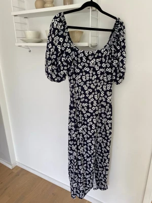 Marinblå långklänning med blommor - Långklänning i marinblått med vitt blommönster och puffiga kortärmar. Slits i ena sidan.