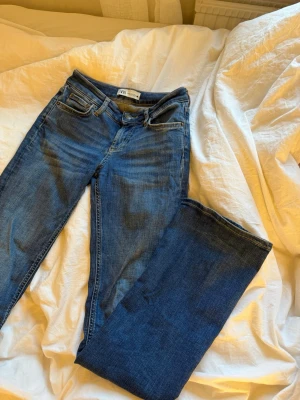 Blå bootcut jeans  - Säljer ett par blå bootcut jeans med klassisk femficksmodell och normalhög midja. Jeansen har en snygg tvätt och raka ben som blir vidare nedtill. Perfekta till en enkel topp eller hoodie.