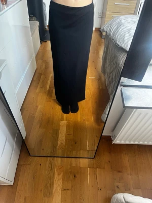 Svart långkjol med rak passform - Säljer en svart långkjol med rak och enkel siluett. Kjolen har hög midja och är i ett mjukt, följsamt material som ger en clean look. Perfekt att styla med crop tops eller stickade tröjor för en trendig vibe.