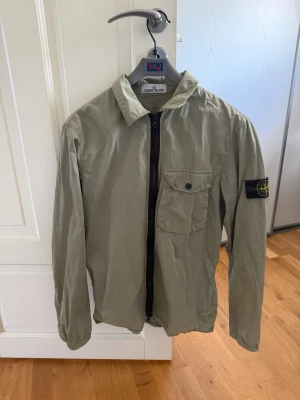 Beige overshirt från Stone Island - Snygg grön overshirt från Stone Island i storleken M. Perfekt nu när hösten faller in.