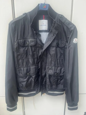 Moncler field jacket - Snygg o stilren moncler field jacket i storlek S/2. Bra skick, bara att en knapp saknas därav priset, inget som märks av vid användning, annars inga defekter. Kom privat för fler frågor✅