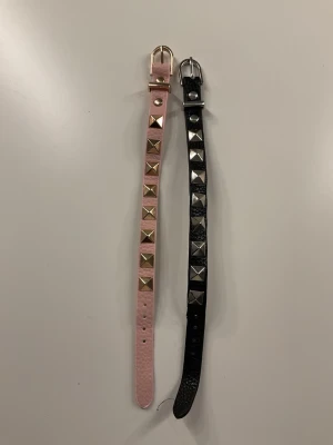 Två armband - Två armband med skinnimitation, ett i ljusrosa och ett i svart. Båda har fyrkantiga metallnitar längs hela bandet och klassiskt metallspänne. Perfekt accessoar för att ge din outfit en cool och edgy vibe.