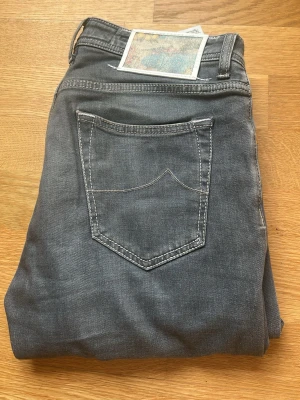 Grå jeans Jacob Cohën ”Napoli” - Snygga grå jeans från Jacob Cohën i Napoli special edition. På baksidan finns en unik patch med Napoli motiv i hästhår, special edition, utöver det guld knappar med Napoli motiv och insida fickor med. Jeansen är i modell Nick och i storlek 32. Knappt använda och väldigt fint skick, riktigt bra läge med en variant som inte kommer tillbaka!