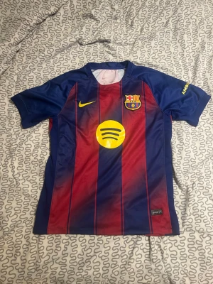 Barcelona matchtröja blå/röd Nike - Säljer en FC Barcelona matchtröja i blått och rött med gula detaljer. Tröjan har klubbmärke, Nike-logga och Spotify-logga på framsidan samt UNHCR-tryck på ryggen. Tillverkad i lätt och ventilerande material, perfekt för fotboll eller träning.