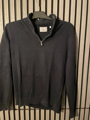 Mörkblå halvzip tröja - Mörkblå tröja med halv dragkedja och ståkrage. Tröjan har långa ärmar och ribbade muddar vid ärmslut och nederkant. Perfekt för lager på lager och enkel att matcha med jeans eller chinos.