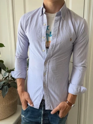  skjorta från Ralph Lauren - Klassisk  skjorta från Ralph Lauren med button-down krage och broderad logga på bröstet. Skjortan har långa ärmar, knappar framtill och är tillverkad i bomull. Perfekt till jeans eller chinos för en clean och stilren look.