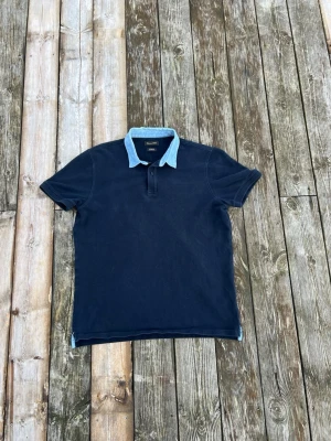 Massimo dutti - Snygg mörkblå pikétröja med korta ärmar och en kontrasterande ljusblå krage. Tröjan har klassisk pikéknäppning framtill och är perfekt för en avslappnad men stilren look.